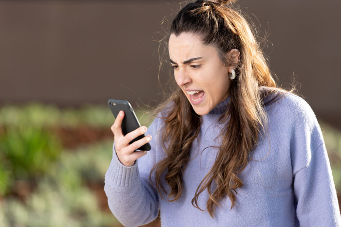 Woman upset with blocked door, angrily speaking on phone, wearing a light sweater in an outdoor setting. Woman upset with blocked door, angrily speaking on phone, wearing a light sweater in an outdoor setting.