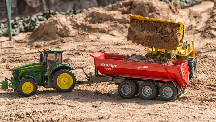 A toy tractor and dump truck in a sandbox, depicting a construction-themed play in a neighbor's yard. A toy tractor and dump truck in a sandbox, depicting a construction-themed play in a neighbor's yard.