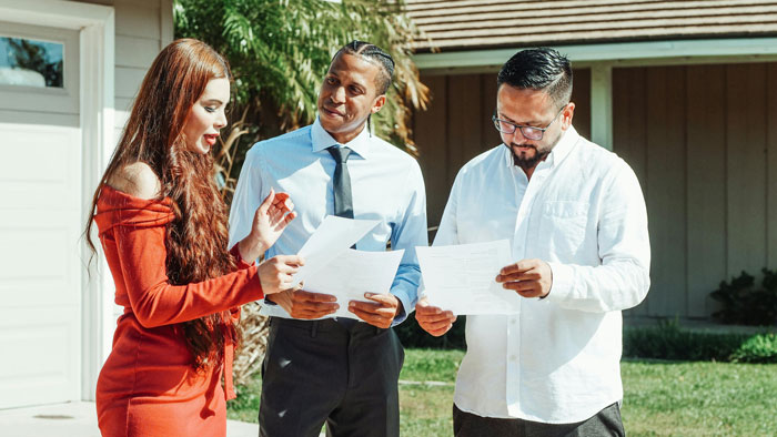 Three people discussing documents in a neighbor's yard, with two men wearing shirts and a woman in a red dress. Three people discussing documents in a neighbor's yard, with two men wearing shirts and a woman in a red dress.