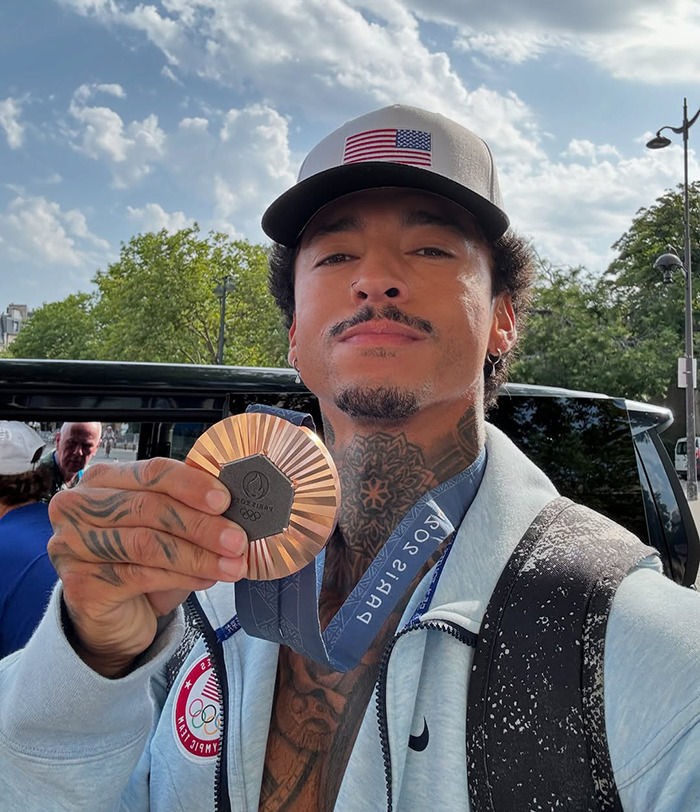 Athlete in Paris holding an Olympic medal outdoors, wearing a cap and light jacket. Athlete in Paris holding an Olympic medal outdoors, wearing a cap and light jacket.