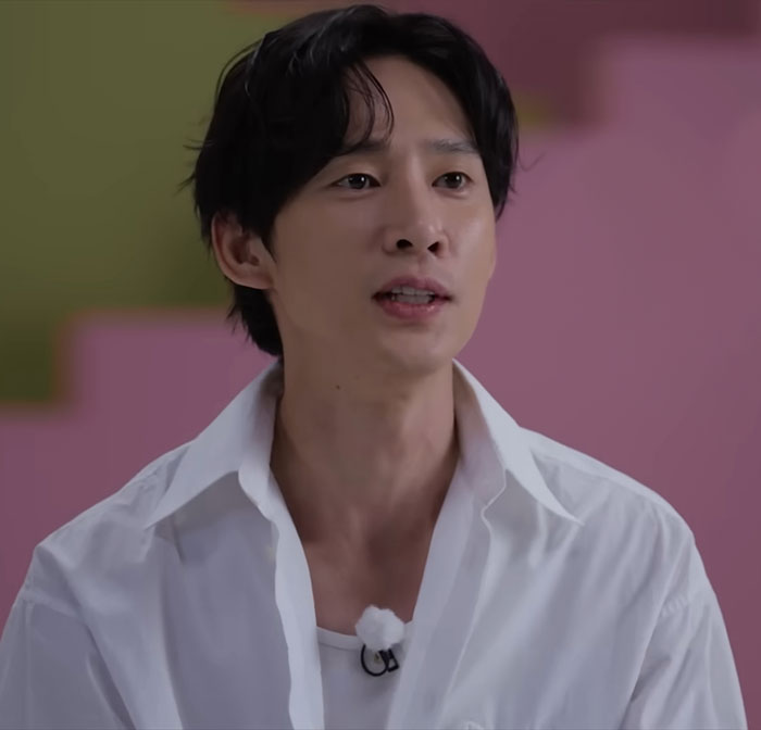 Squid Game actor in a white shirt, expressing apology, with a colorful background. Squid Game actor in a white shirt, expressing apology, with a colorful background.