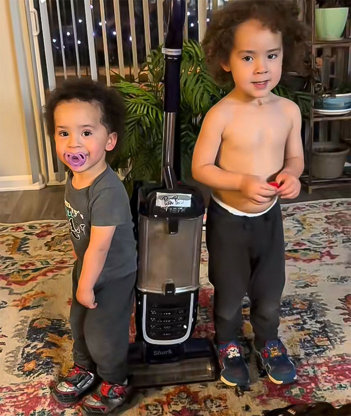 Two young boys standing on a colorful rug beside a vacuum cleaner. Two young boys standing on a colorful rug beside a vacuum cleaner.