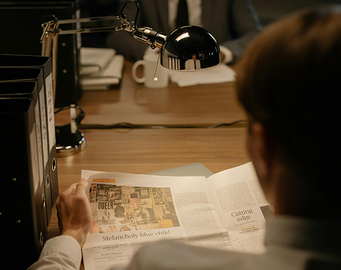 Person reading newspaper at desk under lamp. Person reading newspaper at desk under lamp.