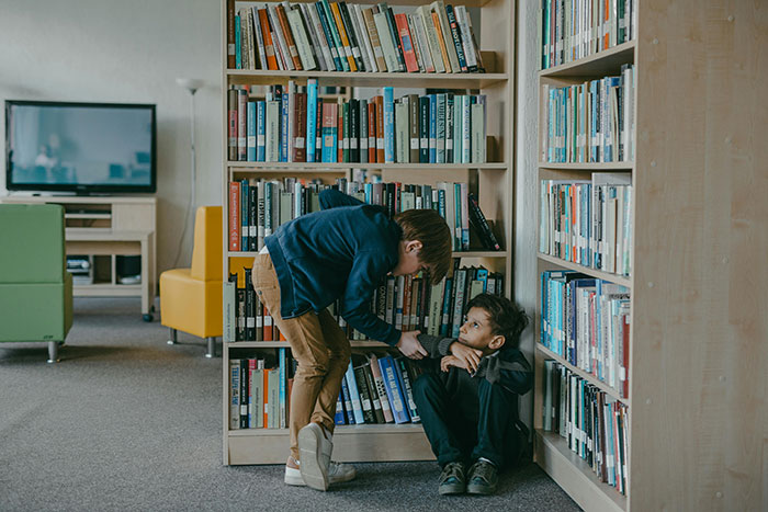 Boy being bullied in a library while sitting near a bookshelf. Boy being bullied in a library while sitting near a bookshelf.