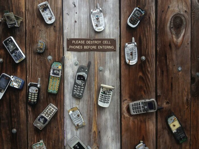 Old cell phones mounted on a wooden wall, reminiscent of teen memories from the 2000s.