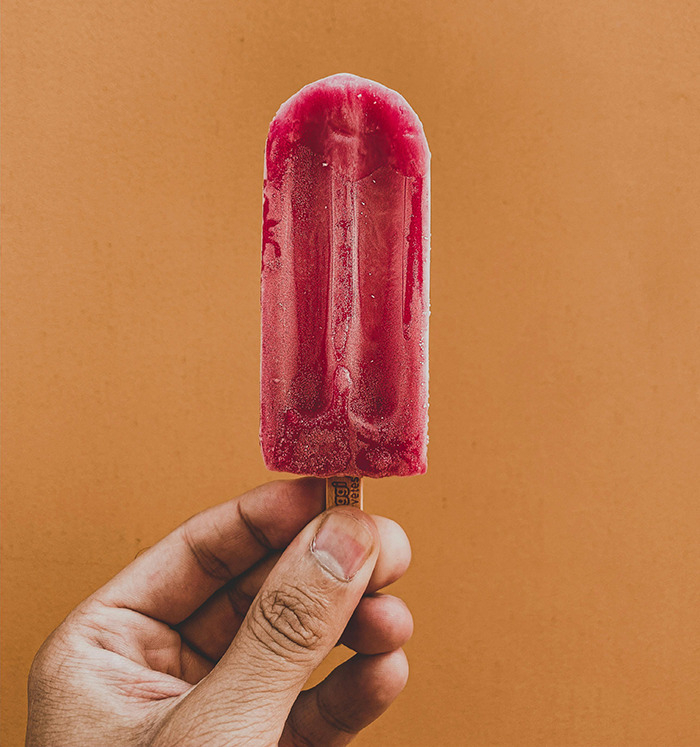 Hand holding a red popsicle, a food often containing artificial color Red Dye No. 3. Hand holding a red popsicle, a food often containing artificial color Red Dye No. 3.