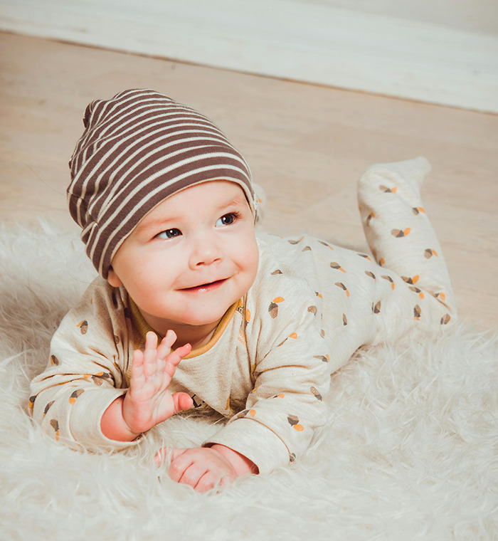 Baby from Generation Beta smiling on a soft rug, wearing a striped hat and patterned outfit. Baby from Generation Beta smiling on a soft rug, wearing a striped hat and patterned outfit.