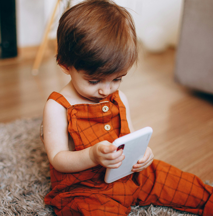 Toddler in orange overalls, engrossed in a smartphone while sitting on a carpet. Toddler in orange overalls, engrossed in a smartphone while sitting on a carpet.