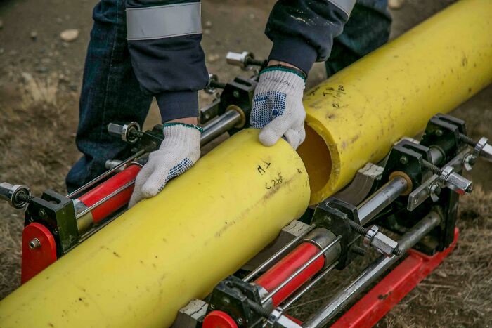 Plumbers handling large yellow pipe with safety gloves in a yard operation. Plumbers handling large yellow pipe with safety gloves in a yard operation.
