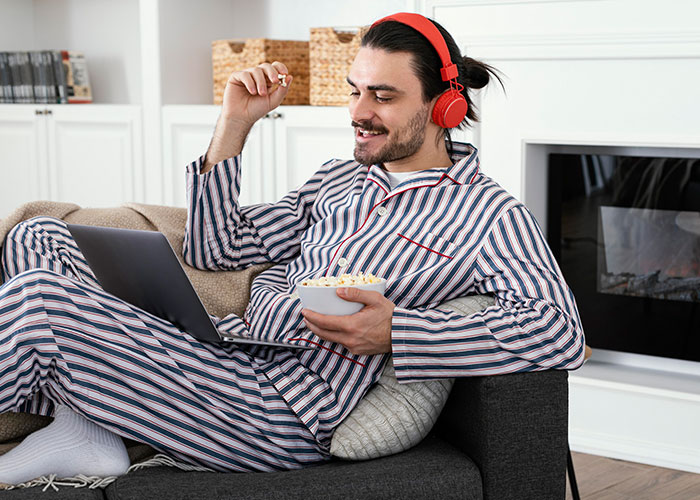 Man in striped pajamas with red headphones watching laptop, symbolizing post-brain rot era relaxation at home. Man in striped pajamas with red headphones watching laptop, symbolizing post-brain rot era relaxation at home.
