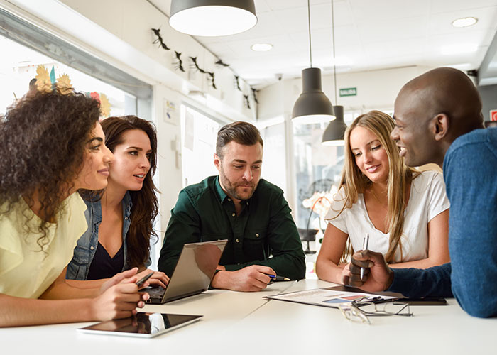 Group discussing post-brain rot era, seated around a table in a modern office, with laptops and documents. Group discussing post-brain rot era, seated around a table in a modern office, with laptops and documents.