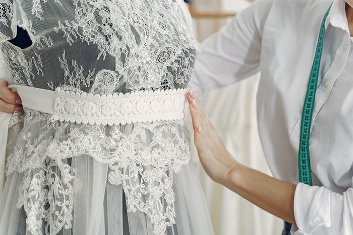 Bridal shop owner adjusting lace on a wedding dress, illustrating a family feud over a second dress request. Bridal shop owner adjusting lace on a wedding dress, illustrating a family feud over a second dress request.