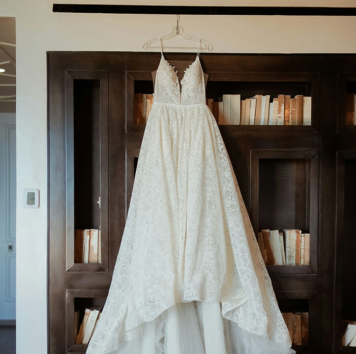 A lace wedding dress hanging in a bridal shop against a bookshelf backdrop. A lace wedding dress hanging in a bridal shop against a bookshelf backdrop.