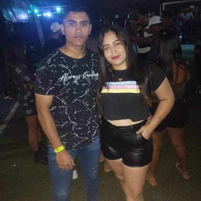 Joyce Sousa Araújo and her partner posing together at a nighttime event, with people in the background. Joyce Sousa Araújo and her partner posing together at a nighttime event, with people in the background.