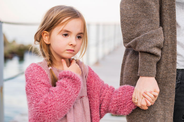 Young girl holding a woman's hand, looking thoughtful outdoors. Young girl holding a woman's hand, looking thoughtful outdoors.