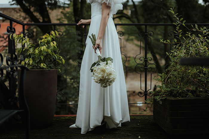 Bride in a white gown holding a bouquet, standing on a balcony with plants, reflecting on wedding decisions. Bride in a white gown holding a bouquet, standing on a balcony with plants, reflecting on wedding decisions.