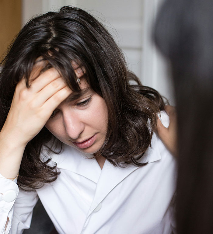 A woman in distress, holding her head, wearing a white shirt, with a comforting hand on her shoulder. A woman in distress, holding her head, wearing a white shirt, with a comforting hand on her shoulder.