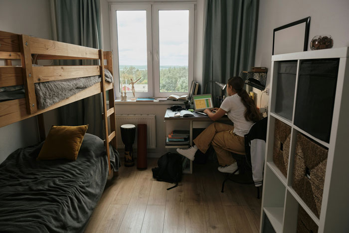 Teen in cozy bedroom with bunk bed and desk, using laptop, faced with parents' request to move to basement for relatives. Teen in cozy bedroom with bunk bed and desk, using laptop, faced with parents' request to move to basement for relatives.