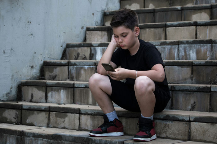 Teen in a dingy basement, sitting on stairs, looking at phone, wearing casual clothes and red sneakers. Teen in a dingy basement, sitting on stairs, looking at phone, wearing casual clothes and red sneakers.