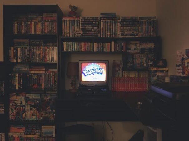 Retro room with shelves of VHS tapes and a small TV playing "Pokemon," evoking nostalgia for good old days.