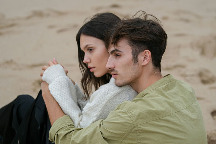 Couple sitting on a sandy beach, embracing closely, capturing a romantic engagement moment. Couple sitting on a sandy beach, embracing closely, capturing a romantic engagement moment.
