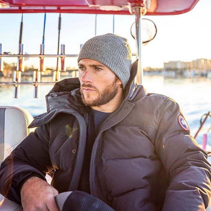 Clint Eastwood's son in a winter jacket and beanie, sitting on a boat, looking contemplative during a sunny day. Clint Eastwood's son in a winter jacket and beanie, sitting on a boat, looking contemplative during a sunny day.