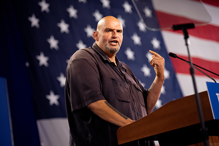 Senator speaking at a podium during a presidential inauguration, wearing casual clothing in front of an American flag. Senator speaking at a podium during a presidential inauguration, wearing casual clothing in front of an American flag.