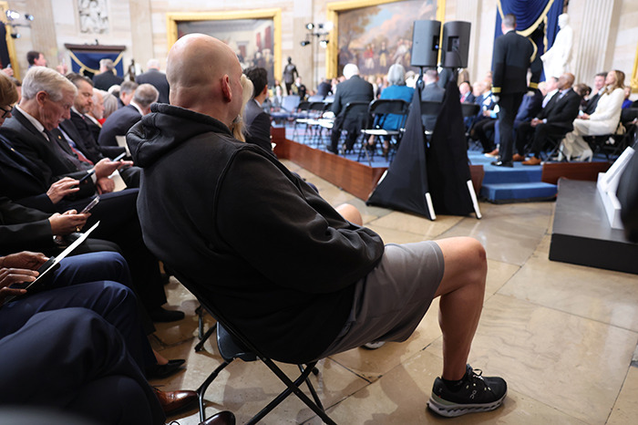 Senator in gym shorts attending a formal presidential inauguration event, seated in a crowded venue. Senator in gym shorts attending a formal presidential inauguration event, seated in a crowded venue.
