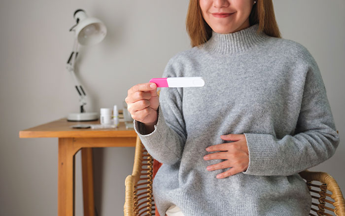 Woman holding a pregnancy test with a smile, touching her belly, announcing pregnancy. Woman holding a pregnancy test with a smile, touching her belly, announcing pregnancy.