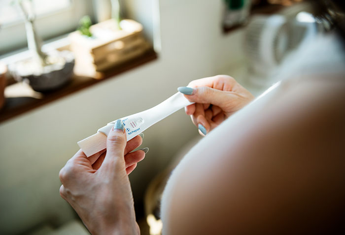 Woman holding a positive pregnancy test by a window, capturing a moment of anticipation and emotion. Woman holding a positive pregnancy test by a window, capturing a moment of anticipation and emotion.