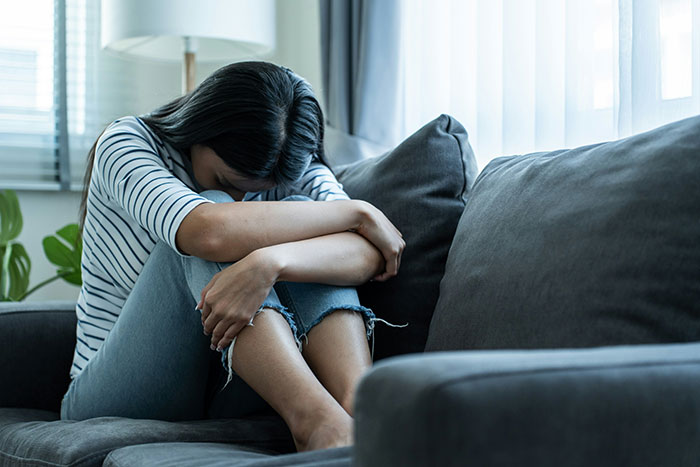 Woman in distress sitting on a couch, concealing her face with knees, struggling with relationship issues. Woman in distress sitting on a couch, concealing her face with knees, struggling with relationship issues.