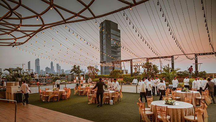 Wedding setup with elegant decor and city skyline, featuring tables and staff preparing for an outdoor event. Wedding setup with elegant decor and city skyline, featuring tables and staff preparing for an outdoor event.
