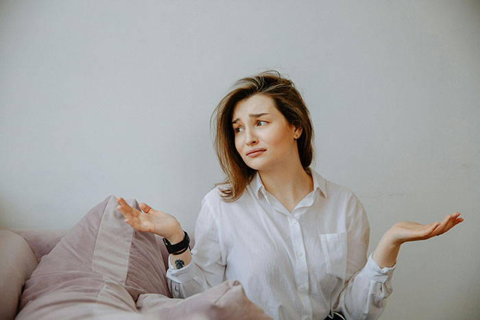A woman in a white shirt sitting on a couch, shrugging, symbolizing a family conflict over an heirloom ring. A woman in a white shirt sitting on a couch, shrugging, symbolizing a family conflict over an heirloom ring.
