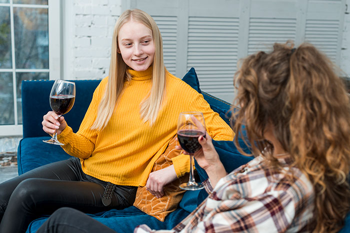 Two sisters having a conversation on a blue couch, each holding a glass of red wine, discussing an heirloom ring. Two sisters having a conversation on a blue couch, each holding a glass of red wine, discussing an heirloom ring.