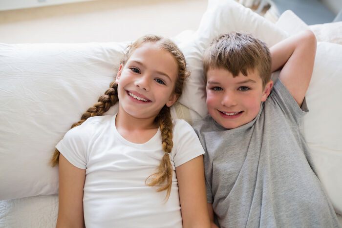Two smiling children lying on pillows, representing a family home setting. Two smiling children lying on pillows, representing a family home setting.