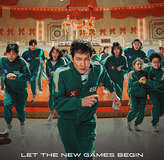 "Squid Game actors in green tracksuits running in a colorful room with carousel horses. "Squid Game actors in green tracksuits running in a colorful room with carousel horses.