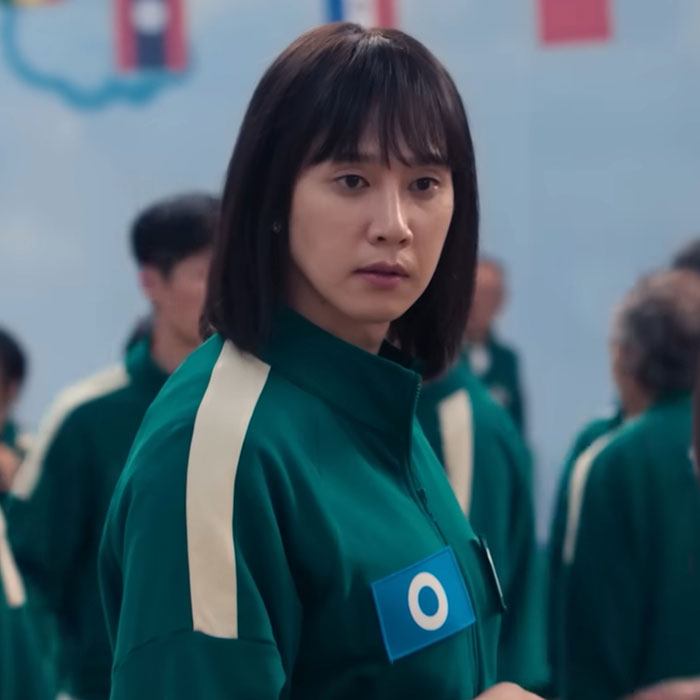Squid Game actor in green tracksuit looking concerned in a crowded room. Squid Game actor in green tracksuit looking concerned in a crowded room.