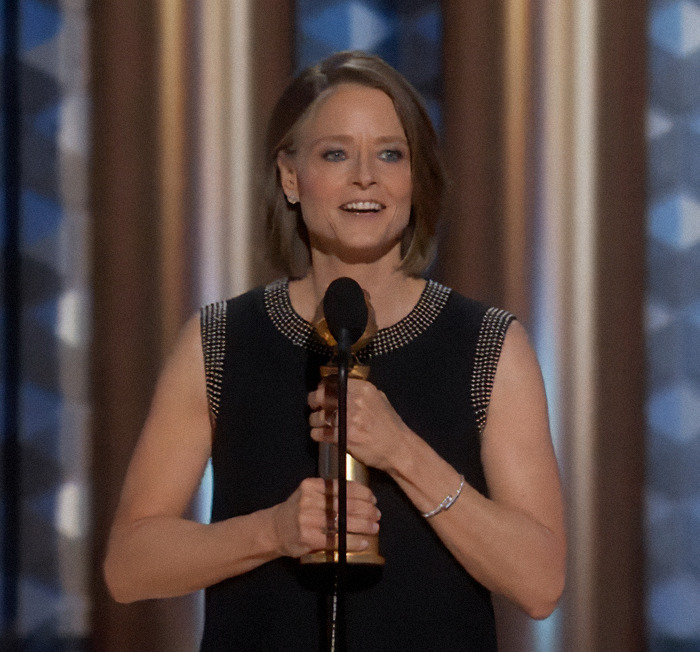 Jodie Foster holding a microphone on stage. Jodie Foster holding a microphone on stage.