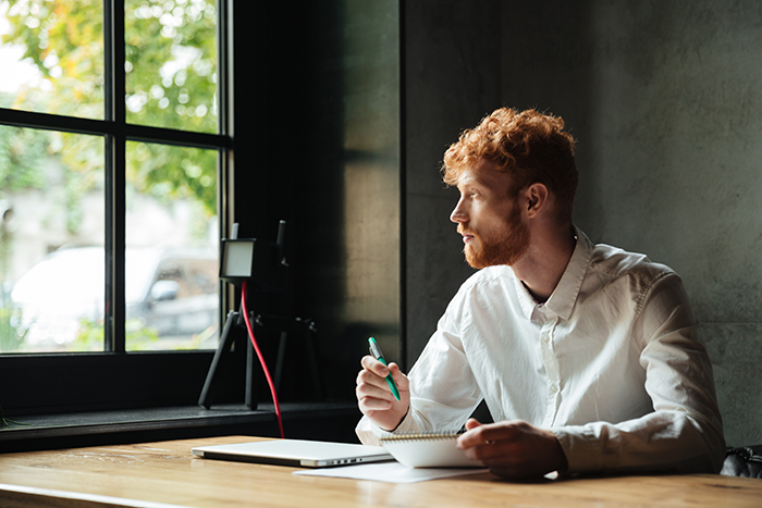 Man in a white shirt, sitting at a desk with notebook, looking thoughtfully out a window. Man in a white shirt, sitting at a desk with notebook, looking thoughtfully out a window.