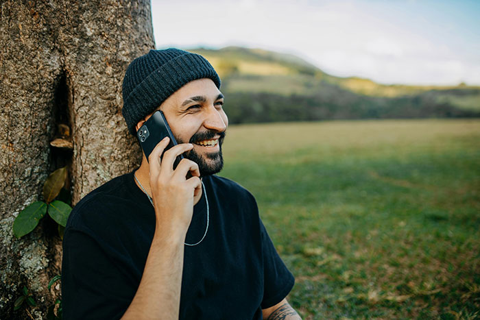 Man smiling and talking on phone outdoors, planning petty revenge on towing company. Man smiling and talking on phone outdoors, planning petty revenge on towing company.