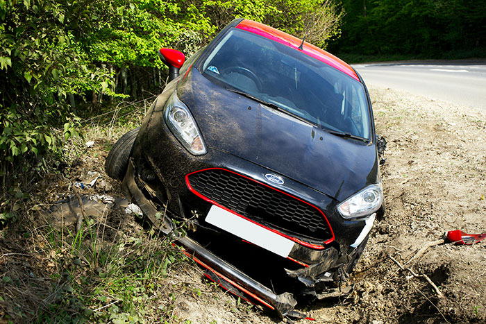 A black car stuck in a ditch with damaged front, surrounded by trees, related to a towing company issue. A black car stuck in a ditch with damaged front, surrounded by trees, related to a towing company issue.