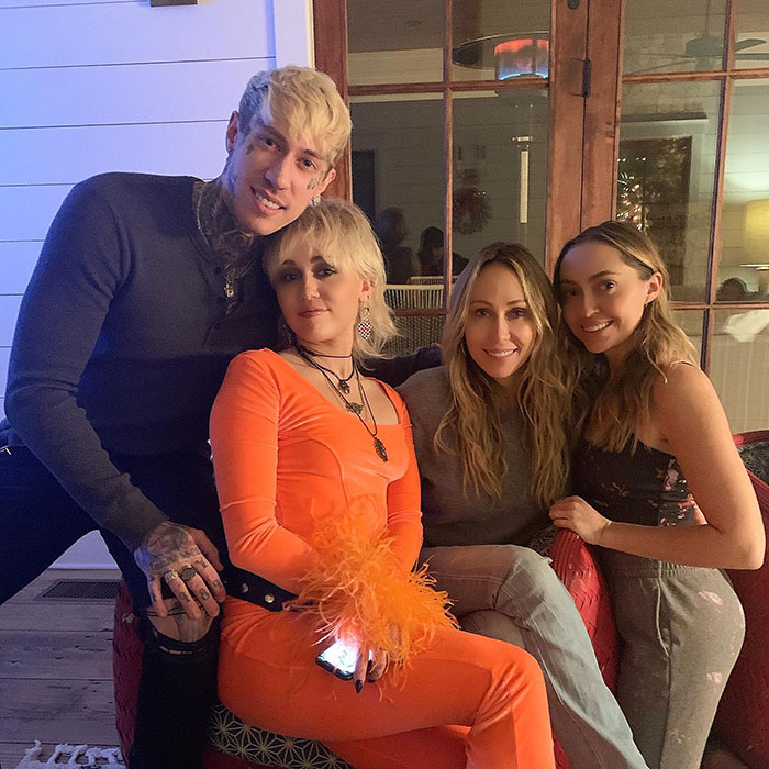 Group of four people sitting together in a cozy home setting, with one person wearing an orange outfit. Group of four people sitting together in a cozy home setting, with one person wearing an orange outfit.