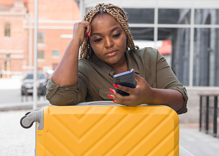 Woman sitting with a suitcase, looking at her phone, reflecting on friendship during a trip. Woman sitting with a suitcase, looking at her phone, reflecting on friendship during a trip.