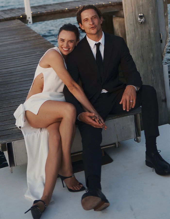 Australian bride in white dress sitting by a dock with groom, holding hands and smiling. Australian bride in white dress sitting by a dock with groom, holding hands and smiling.