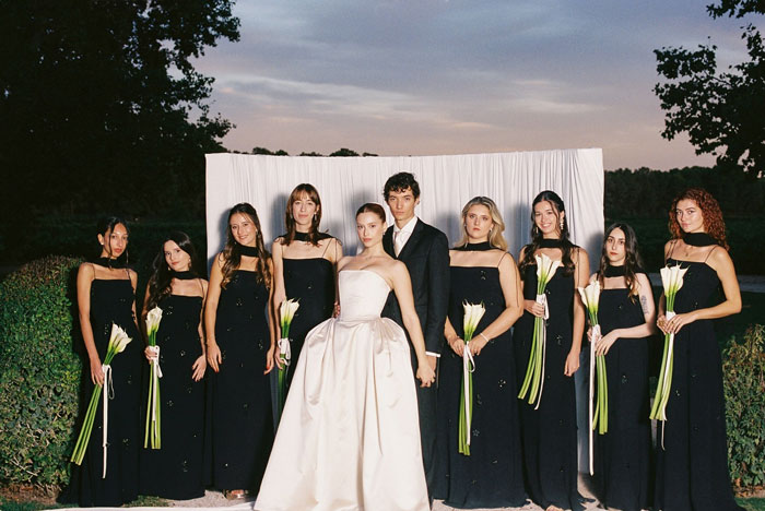Bridal party posing, bride in a dramatic wedding dress and veil, with bridesmaids in black dresses holding white flowers. Bridal party posing, bride in a dramatic wedding dress and veil, with bridesmaids in black dresses holding white flowers.