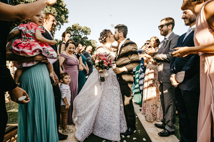 Wedding celebration with bride and groom kissing, surrounded by guests in colorful attire, outdoors on a sunny day. Wedding celebration with bride and groom kissing, surrounded by guests in colorful attire, outdoors on a sunny day.