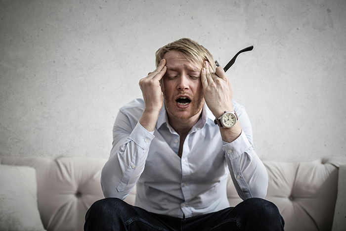 Man in distress on a sofa, wearing a white shirt and holding his head, embodying issues with keeping privacy. Man in distress on a sofa, wearing a white shirt and holding his head, embodying issues with keeping privacy.