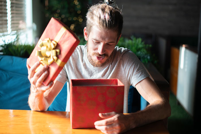 Man looking upset while opening an expensive gift at a table, seeking advice. Man looking upset while opening an expensive gift at a table, seeking advice.