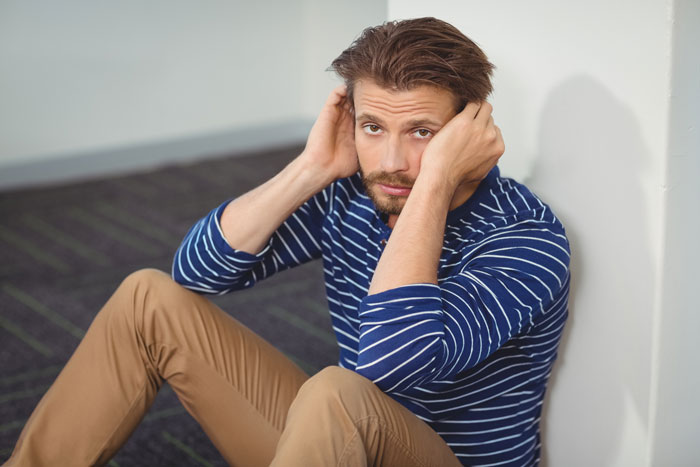 Man sitting on floor in a striped shirt, looking frustrated, related to fixing family attitude issues. Man sitting on floor in a striped shirt, looking frustrated, related to fixing family attitude issues.