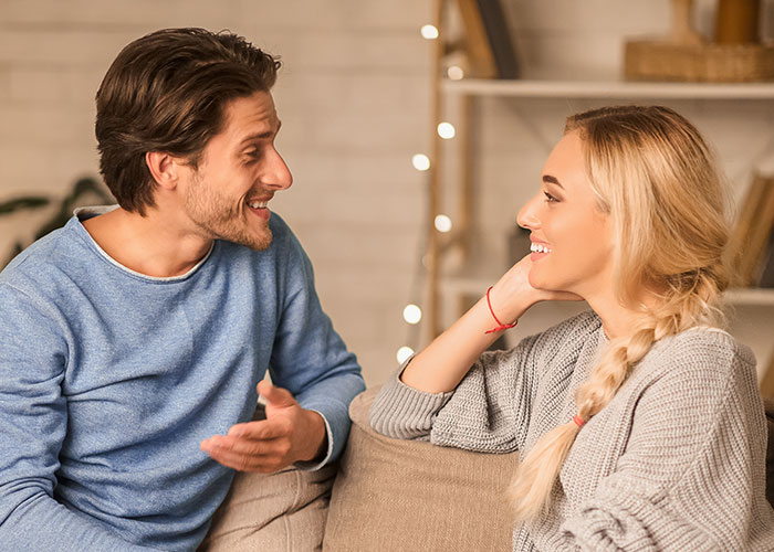 Couple smiling and chatting on a cozy sofa, discussing a public proposal turned private conversation. Couple smiling and chatting on a cozy sofa, discussing a public proposal turned private conversation.